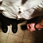 Chef wearing chef coat and black pants looking down at his black Mozo Chef Shoes while standing in a sand tiled kitchen. 